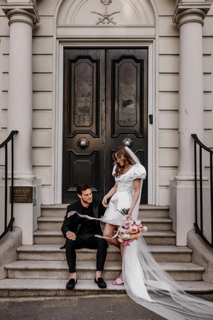 Photographer: Emma Wilder. Modern couple, short wedding dress, large shoulders, long veil. pink wedding shoes.