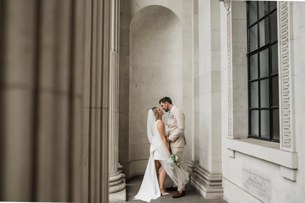 Photographer: Katie Rogers. Modern bride and groom, town hall wedding ceremony, short bridal dress, beige grooms suit.