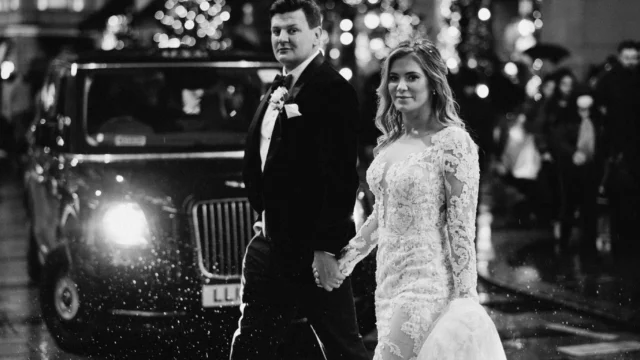 Photographer: Olegs and Rita Photography. Modern London Bride and groom crossing the road, black London cab.