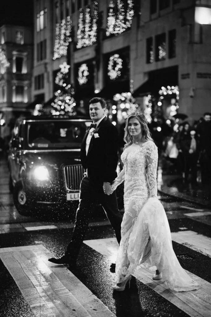 Photographer: Olegs and Rita Photography. Modern London Bride and groom crossing the road, black London cab.